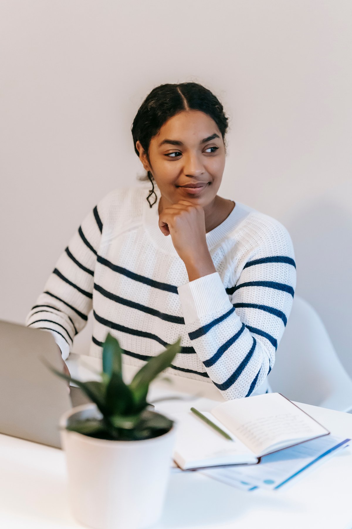 Ethnic woman working remotely on netbook near notebook in room